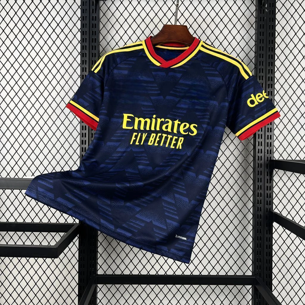 Camiseta Arsenal 26-27 visitante vista frontal en azul marino con patrón geométrico tonal, cuello rojo y amarillo y detalles amarillos en hombros