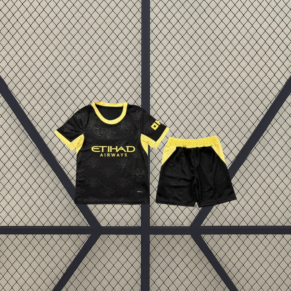 Equipación Manchester City 26-27 Visitante de niño con camiseta y pantalón negros, patrón de abejas y detalles amarillos