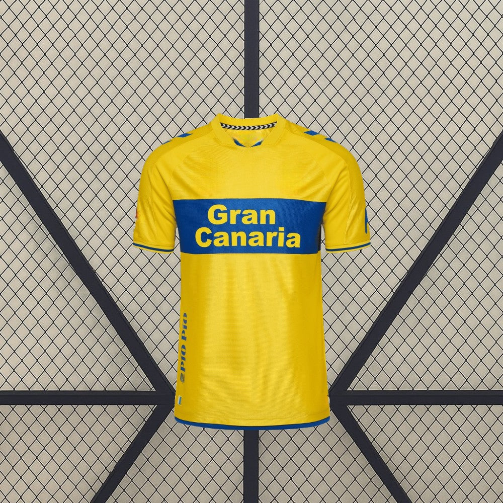 Vista frontal centrada de la camiseta Las Palmas 26-27 local en amarillo, con banda azul horizontal, cuello redondo y detalles azules