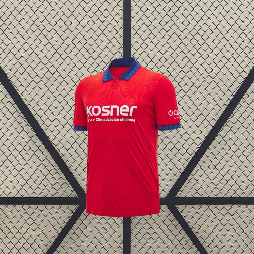 Vista frontal de la camiseta Osasuna 26-27 local en rojo, con cuello tipo polo azul, puños estampados y patrón tonal en el pecho