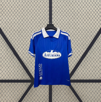 Vista frontal de la camiseta Real Oviedo 26-27 local en azul, con cuello tipo polo blanco, manga corta y detalles blancos en los hombros