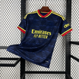 Camiseta Arsenal 26-27 visitante vista frontal en azul marino con patrón geométrico tonal, cuello rojo y amarillo y detalles amarillos en hombros