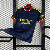 Camiseta Arsenal 26-27 visitante vista frontal en azul marino con patrón geométrico tonal, cuello rojo y amarillo y detalles amarillos en hombros