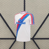 Camiseta Crystal Palace 26-27 local vista frontal en blanco con franjas diagonales rojas y azules y cuello redondo