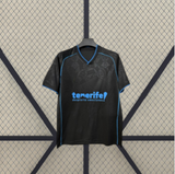Camiseta Tenerife 26-27 visitante vista frontal desplegada en negro con patrón tonal y detalles azul turquesa en cuello y mangas