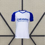 Camiseta Zaragoza 26-27 local vista frontal en blanco con mangas azules, hombros a contraste y cuello con ribete azul