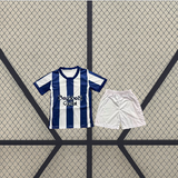 Conjunto infantil Real Sociedad 26-27 local con camiseta de franjas verticales azules y blancas y pantalón corto blanco presentado en plano frontal