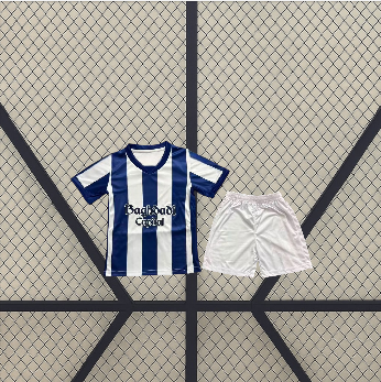 Conjunto infantil Real Sociedad 26-27 local con camiseta de franjas verticales azules y blancas y pantalón corto blanco presentado en plano frontal