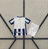 Conjunto infantil Real Sociedad 26-27 local visto por detrás con camiseta blanca, franjas azules inferiores y pantalón corto blanco