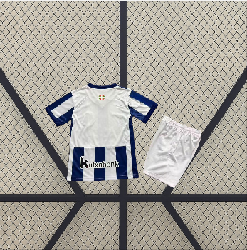 Conjunto infantil Real Sociedad 26-27 local visto por detrás con camiseta blanca, franjas azules inferiores y pantalón corto blanco