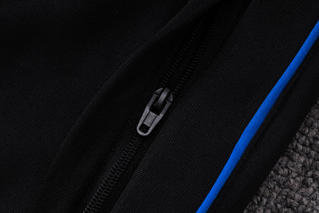 Detalle de la cremallera frontal y del ribete azul sobre fondo negro en el chándal PSG 26-27 Modelo 1