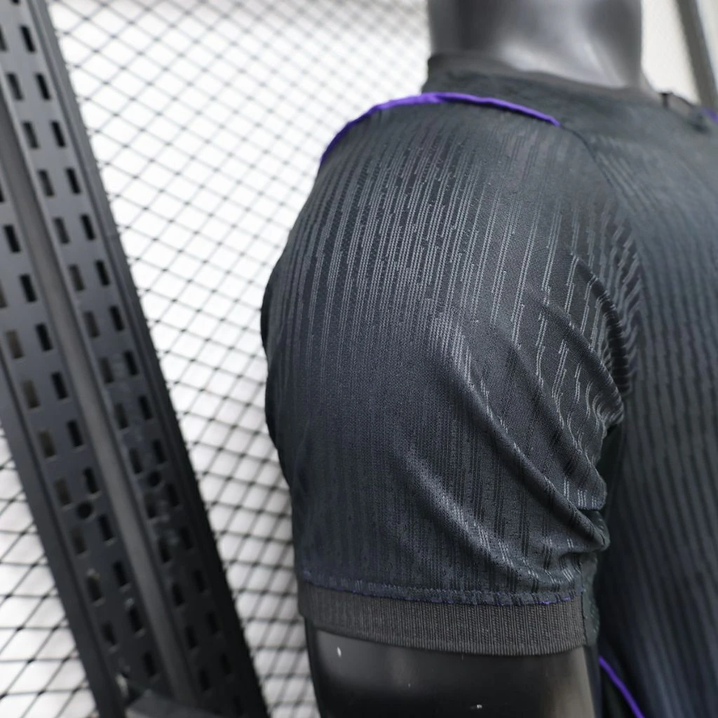 Detalle de la manga y el hombro de la camiseta Barcelona 26-27 visitante Player con tejido negro texturizado, puño y ribete morado