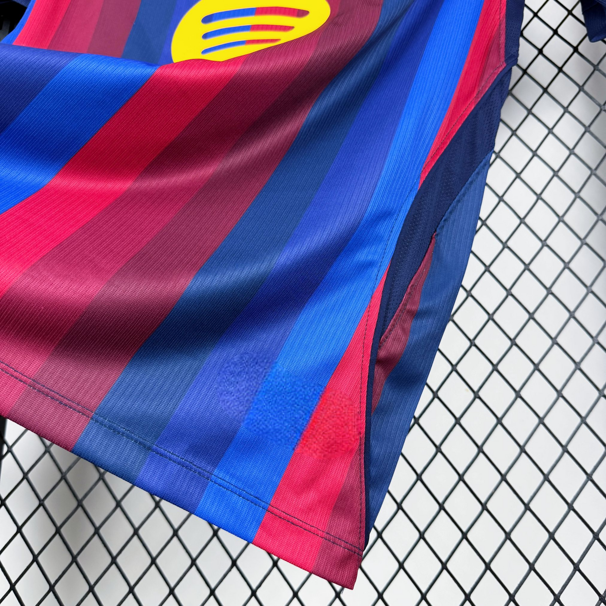 Detalle del tejido y panel lateral de malla de la camiseta Barcelona 26-27 local, con franjas azulgranas y dobladillo cosido