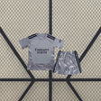 Equipación Arsenal 26-27 portero gris niño vista frontal con camiseta gris clara, detalles oscuros en hombros y pantalón corto gris con franjas laterales