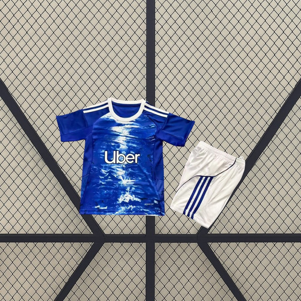 Equipación Como 25-26 local para niño vista frontal con camiseta azul de gráfico blanco y pantalón corto blanco