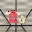 Equipación Málaga 26-27 visitante infantil con camiseta rosa y crema de detalles geométricos y pantalón corto crema con acabados granates