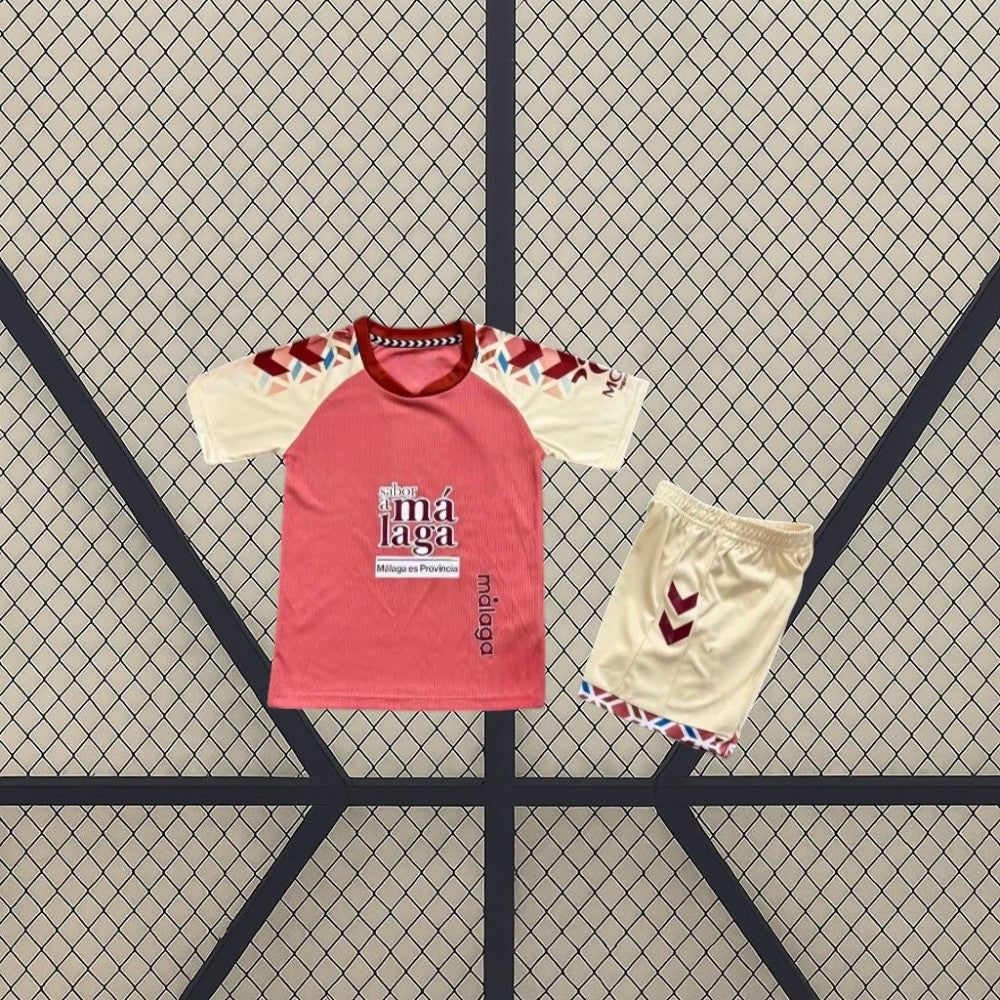 Equipación Málaga 26-27 visitante infantil con camiseta rosa y crema de detalles geométricos y pantalón corto crema con acabados granates