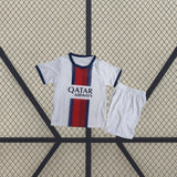 Equipación PSG 26-27 visitante niño vista frontal con camiseta blanca, franja central azul marino y roja y pantalón blanco