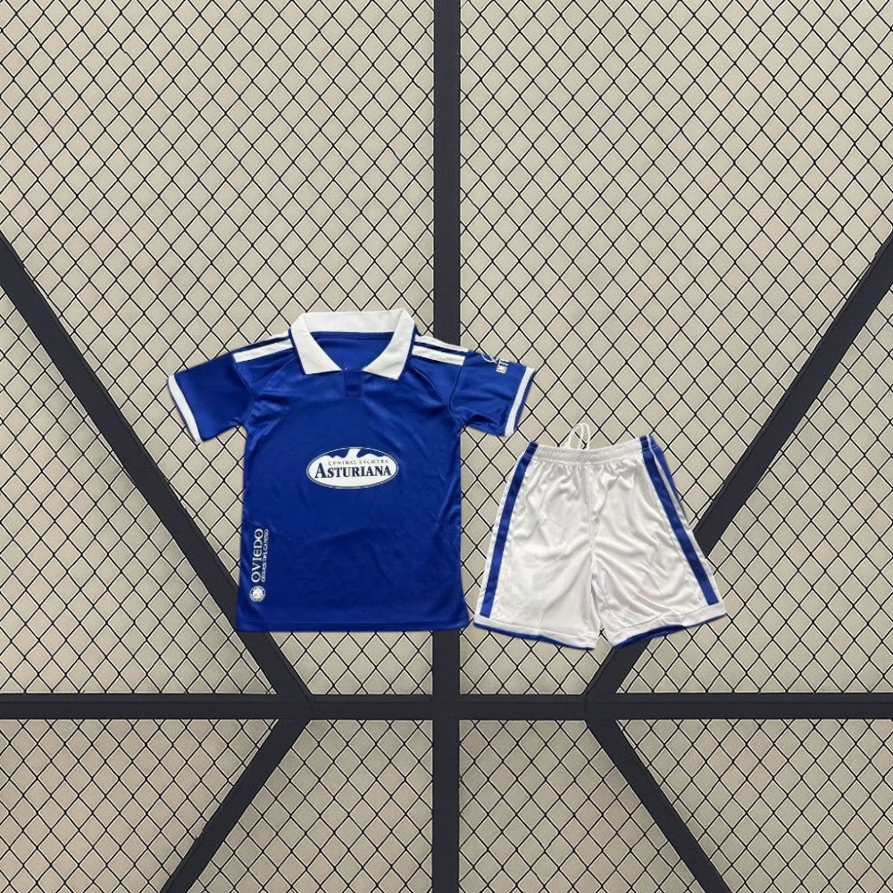 Equipación Real Oviedo 26-27 local infantil con camiseta azul de cuello polo blanco y pantalón corto blanco con franjas laterales azules
