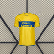 Vista frontal centrada de la camiseta Las Palmas 26-27 local en amarillo, con banda azul horizontal, cuello redondo y detalles azules