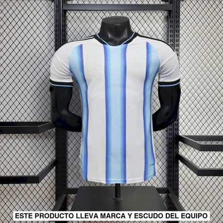 Vista frontal de la camiseta Argentina 26-27 local versión Player, blanca con franjas celestes degradadas, cuello negro y manga corta