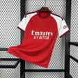 Vista frontal de la camiseta Arsenal 26-27 local con cuerpo rojo, mangas blancas, detalles granate y CLIMACOOL visible junto al bajo