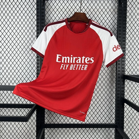 Vista frontal de la camiseta Arsenal 26-27 local con cuerpo rojo, mangas blancas, detalles granate y CLIMACOOL visible junto al bajo