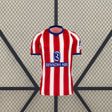 Vista frontal de la camiseta Atlético de Madrid 26-27 local con franjas verticales rojas y blancas, cuello azul y manga corta