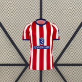 Vista frontal de la camiseta Atlético de Madrid 26-27 local con franjas verticales rojas y blancas, cuello azul y manga corta