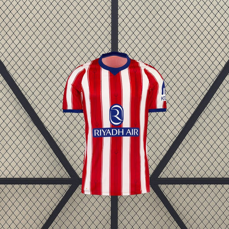 Vista frontal de la camiseta Atlético de Madrid 26-27 local con franjas verticales rojas y blancas, cuello azul y manga corta