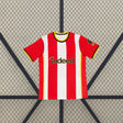Vista frontal de la camiseta Brentford 26-27 local con franjas verticales rojas y blancas, cuello redondo y detalles amarillos y negros