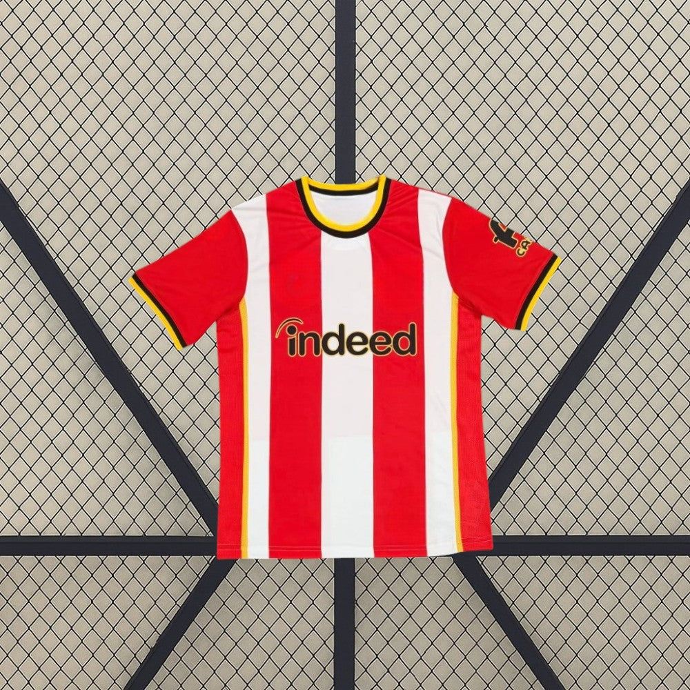 Vista frontal de la camiseta Brentford 26-27 local con franjas verticales rojas y blancas, cuello redondo y detalles amarillos y negros