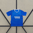Vista frontal de la camiseta Brighton 26-27 Local azul con finas líneas verticales, mangas cortas y cuello redondo con borde blanco