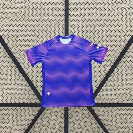 Vista frontal de la camiseta Elche 26-27 Visitante en azul y violeta con patrón gráfico ondulado, cuello redondo y manga corta