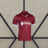 Vista frontal de la camiseta Getafe 26-27 visitante en color granate, con cuello en pico, puños blancos y patrón tonal geométrico
