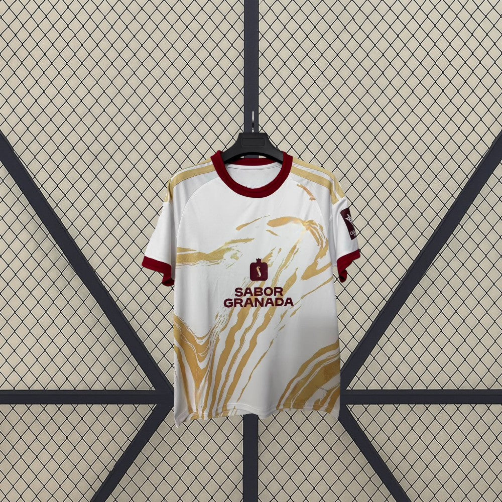 Vista frontal de la camiseta Granada 26-27 tercera equipación en blanco con gráfico dorado y cuello redondo granate