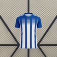 Vista frontal de la camiseta Huelva 26-27 Local con franjas verticales azules y blancas, cuello redondo y mangas azules