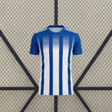Vista frontal de la camiseta Huelva 26-27 Local con franjas verticales azules y blancas, cuello redondo y mangas azules