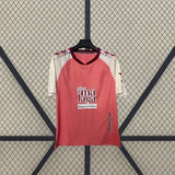 Vista frontal de la camiseta Málaga 26-27 visitante colgada, con base coral, mangas crema y detalles geométricos multicolor en los hombros