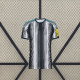 Vista frontal de la camiseta Newcastle 26-27 local con franjas verticales blancas y negras, cuello redondo y detalles azul celeste