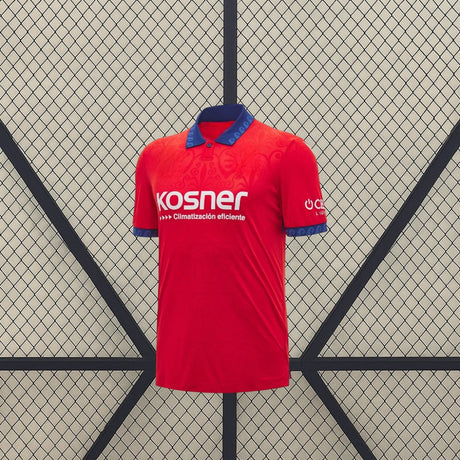 Vista frontal de la camiseta Osasuna 26-27 local en rojo, con cuello tipo polo azul, puños estampados y patrón tonal en el pecho