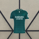 Vista frontal de la camiseta R.M. 26-27 visitante en verde oscuro, con patrón tonal, cuello abierto con ribete blanco y manga corta