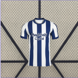 Vista frontal de la camiseta Real Sociedad 26-27 local con franjas verticales blancas y azul marino, cuello redondo y manga corta