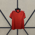 Vista frontal de la camiseta Sevilla 26-27 visitante en color rojo, con cuello tipo polo negro, franjas blancas en los hombros y manga corta