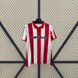 Vista frontal de la camiseta Sporting de Gijón 26-27 local con franjas verticales rojas y blancas, cuello tipo polo y manga corta