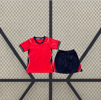 Vista frontal de la equipación Inglaterra 26-27 visitante para niño con camiseta roja, detalles azul marino y pantalón corto a juego