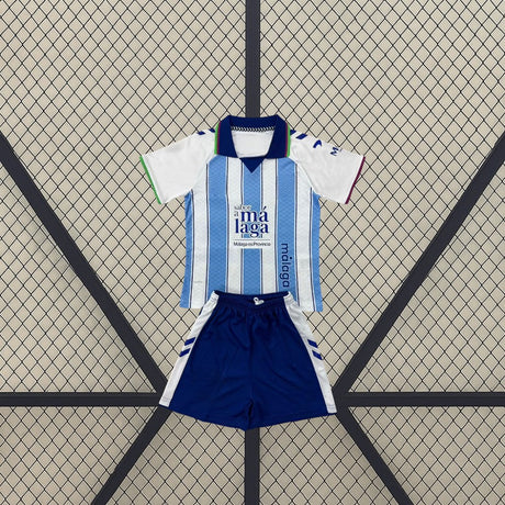 Vista frontal de la equipación Málaga niño 26-27 local con camiseta blanca y azul claro y pantalón azul marino