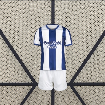 Vista frontal de la equipación Real Sociedad 26-27 local para niño con camiseta de franjas azules y blancas y pantalón corto blanco
