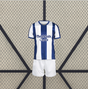 Vista frontal de la equipación Real Sociedad 26-27 local para niño con camiseta de franjas azules y blancas y pantalón corto blanco