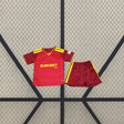 Vista frontal de la equipación Roma 26-27 local para niño con camiseta granate, detalles amarillos y pantalón corto granate con franja amarilla